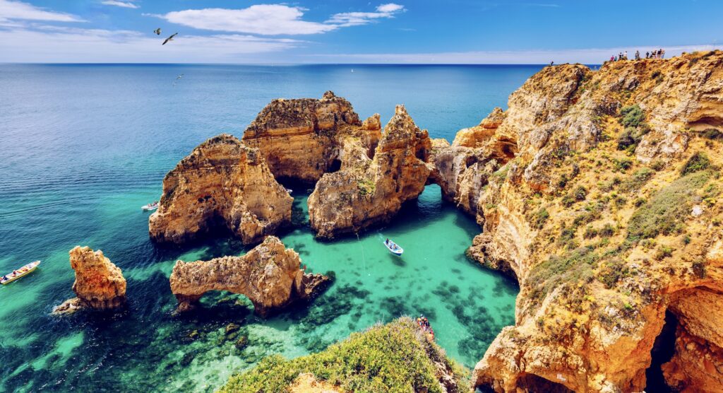 Panoramic view, Ponta da Piedade with seagulls flying over rocks near Lagos in Algarve, Portugal. Cliff rocks, seagulls and tourist boat on sea at Ponta da Piedade, Algarve region, Portugal.